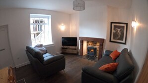 A modern living room with a fireplace, two sofas, a television, and a large window. - Albert Cottage, Skipton (Skipton)
