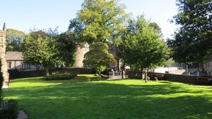 A courtyard with a lawn, a stone wall, and a building with arched windows. - Albert Cottage, Skipton (Skipton)