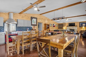 A rustic kitchen with wooden beams, a gas stove, and a dining area with wooden chairs. - Miracle Lodge | Pool, Hot Tub & Scenic Views (Leakey)
