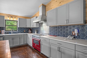 A modern kitchen with grey cabinets, a red oven, and a hexagonal tile backsplash. - Miracle Lodge | Pool, Hot Tub & Scenic Views (Leakey)