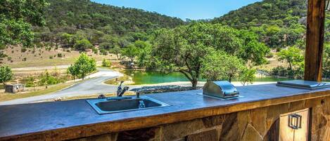 Una barra de piedra con pileta y parrilla, con vista a un lago y colinas boscosas.
