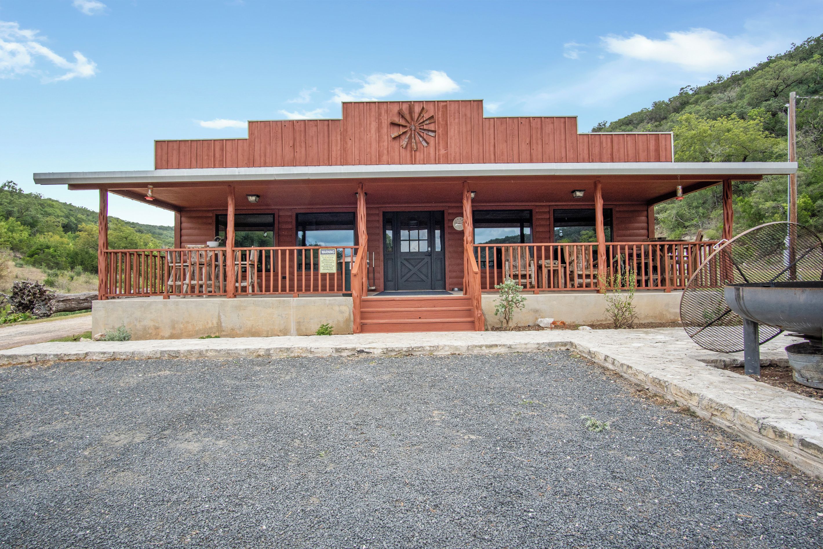A two-story building with a front porch, a windmill on the roof, and a gravel driveway.