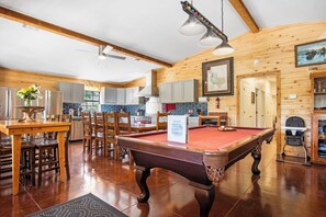 A wooden interior with a pool table, dining area, kitchen, and a map on the wall. - Miracle Lodge | Pool, Hot Tub & Scenic Views (Leakey)