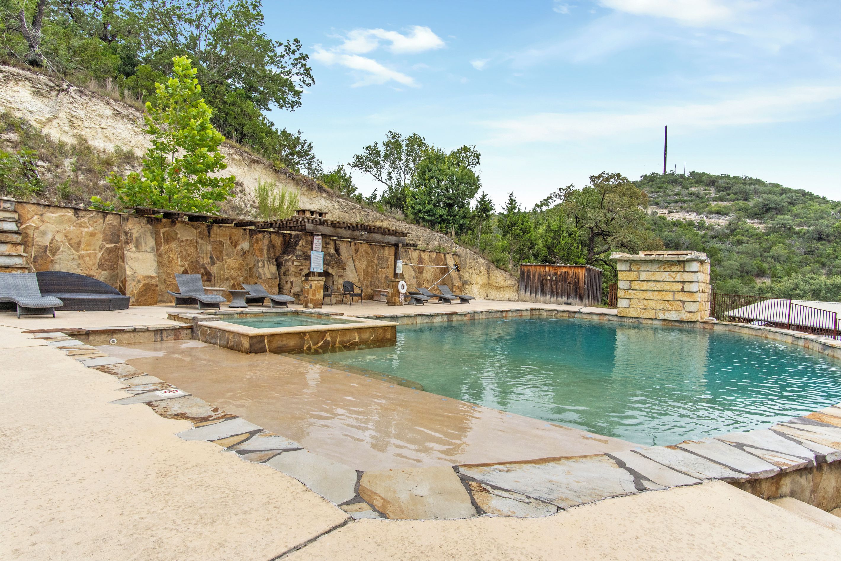 Une piscine aux murs et au bord en pierre, entourée d’un mur en pierre et d’une clôture en bois.