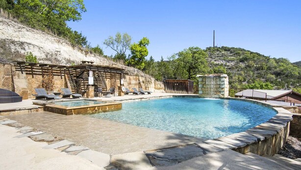 Una piscina con sillas de descanso y una cascada, rodeada de muros de piedra y vegetación.
