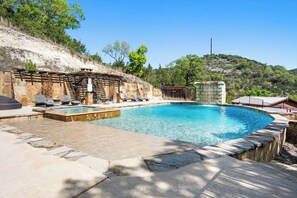 A swimming pool with lounge chairs and a stone wall. - Miracle Lodge | Pool, Hot Tub & Scenic Views (Leakey)