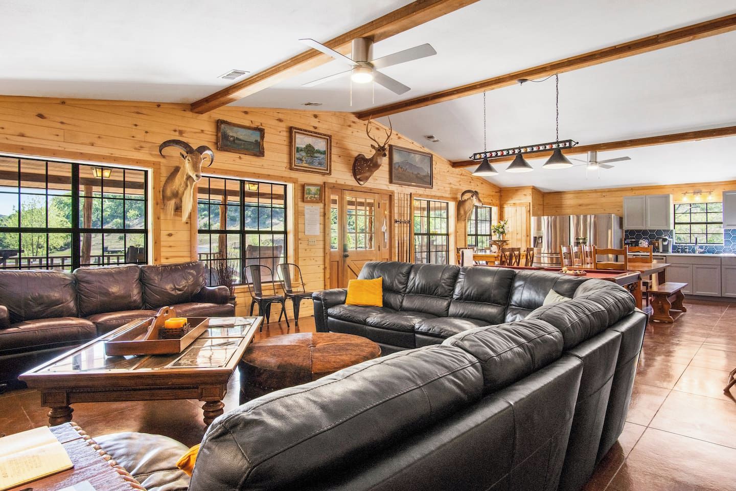 A spacious living area with leather sofas, a dining table, and a kitchen in the background.