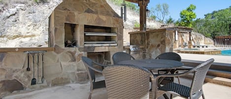 Eine Terrasse im Freien mit Steinmauern, einem Steinofen und Korbmöbeln.
