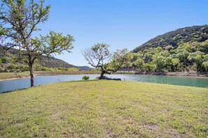 A grassy area with a body of water and trees. - Miracle Lodge | Pool, Hot Tub & Scenic Views (Leakey)