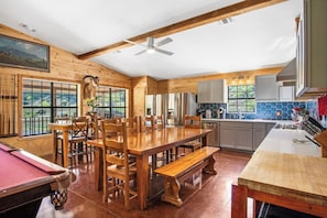 A spacious kitchen with wooden cabinets, a large island, and a dining area with a pool table. - Miracle Lodge | Pool, Hot Tub & Scenic Views (Leakey)