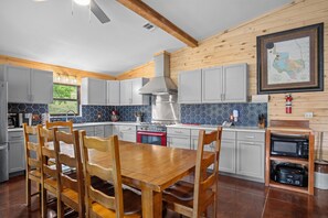 A modern kitchen with a wooden dining table and chairs, a red oven, and a map on the wall. - Miracle Lodge | Pool, Hot Tub & Scenic Views (Leakey)