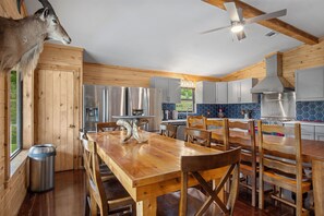 A modern kitchen with wooden accents, stainless steel appliances, and a dining area with a unique animal-themed table base. - Miracle Lodge | Pool, Hot Tub & Scenic Views (Leakey)