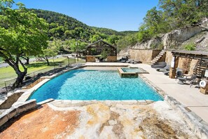 A swimming pool with a stone deck, lounge chairs, and a wooden structure in the background. - Miracle Lodge | Pool, Hot Tub & Scenic Views (Leakey)