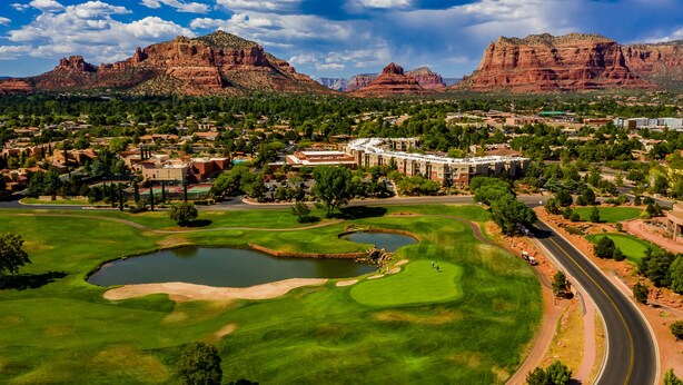 A golf course with a pond, surrounded by residential buildings and red rock formations.
