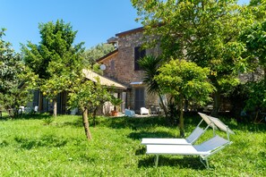 A stone house with a garden, outdoor seating, and a white lounge chair. - Domus Acqua Viva (massa lubrense)