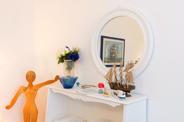 A room with a white vanity, a wooden ship model, a vase with flowers, and a small figurine. - Domus Acqua Viva (massa lubrense)