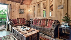 Et interiør af en træhytte med en stor sofa, et sofabord og et skilt med teksten "Welcome to Cabin".