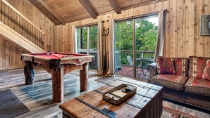 Et træinteriør med et billardbord, en sofa og en balkon med udsigt til træer.