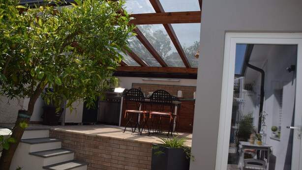 A patio with a brick wall, a wooden table with chairs, and a large potted plant. - La Quintecita villa with private pool -near Catania and Etna (San Giovanni La Punta)