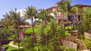 Un resort con un sendero que conduce a un edificio con balcón, rodeado de abundante vegetación y palmeras.