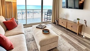 A living room with a sofa, ottoman, and a TV on the wall. - Don’t Worry, Beach Happy! 3rd Floor Beachfront Condo @ Majestic ~ Sleeps 8 (Panama City Beach)