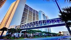 A modern urban street with a pedestrian overpass, tall buildings, and palm trees. - Don’t Worry, Beach Happy! 3rd Floor Beachfront Condo @ Majestic ~ Sleeps 8 (Panama City Beach)