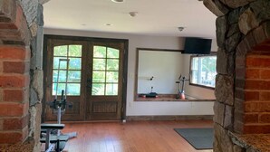 Una habitación con arco de piedra, suelo de madera, equipo de ejercicio, una ventana con vistas y un televisor montado.