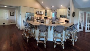 Una cocina amplia con una isla central, muebles blancos y una zona de bar con sillas de mimbre.