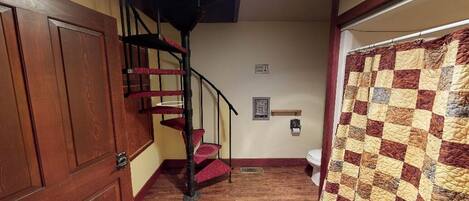 A staircase with a red carpet, a wooden door, a quilted curtain, and a framed picture on the wall.