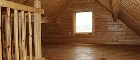 Un dormitorio en el ático con paredes y suelo de madera, una ventana con vistas y una escalera de madera.