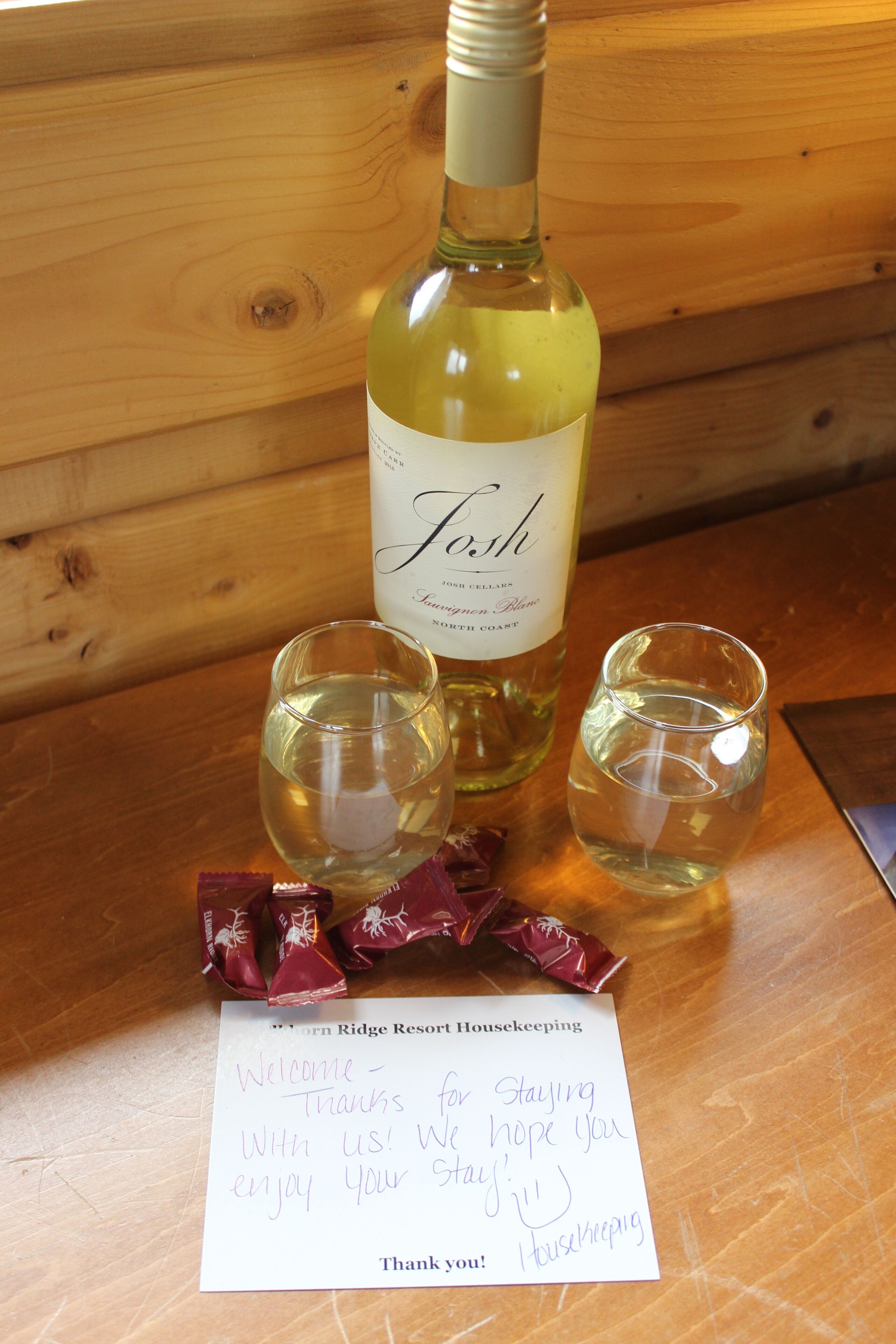 A bottle of white wine, two shot glasses, and a handwritten note on a wooden table.