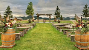 A rustic outdoor wedding venue with wooden benches and barrels, a wooden archway, and a grassy path. - Elkhorn Ridge Resort (Spearfish)