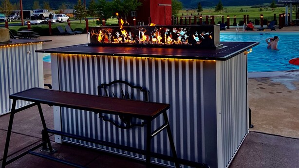 An outdoor bar area with a pool, a red building, and a view of mountains. - Elkhorn Ridge Resort (Spearfish)