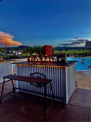 An outdoor bar area with a pool, a red building, and a view of mountains.