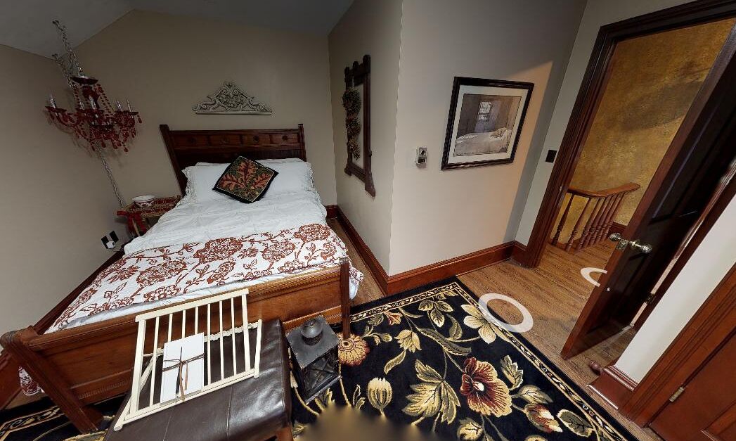 A bedroom with a wooden bed, a chandelier, a framed picture, and a door leading to another room.