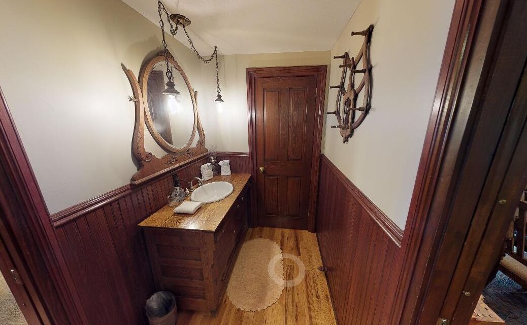 A narrow bathroom with wooden paneling, a wooden door, a mirror, and a sink.