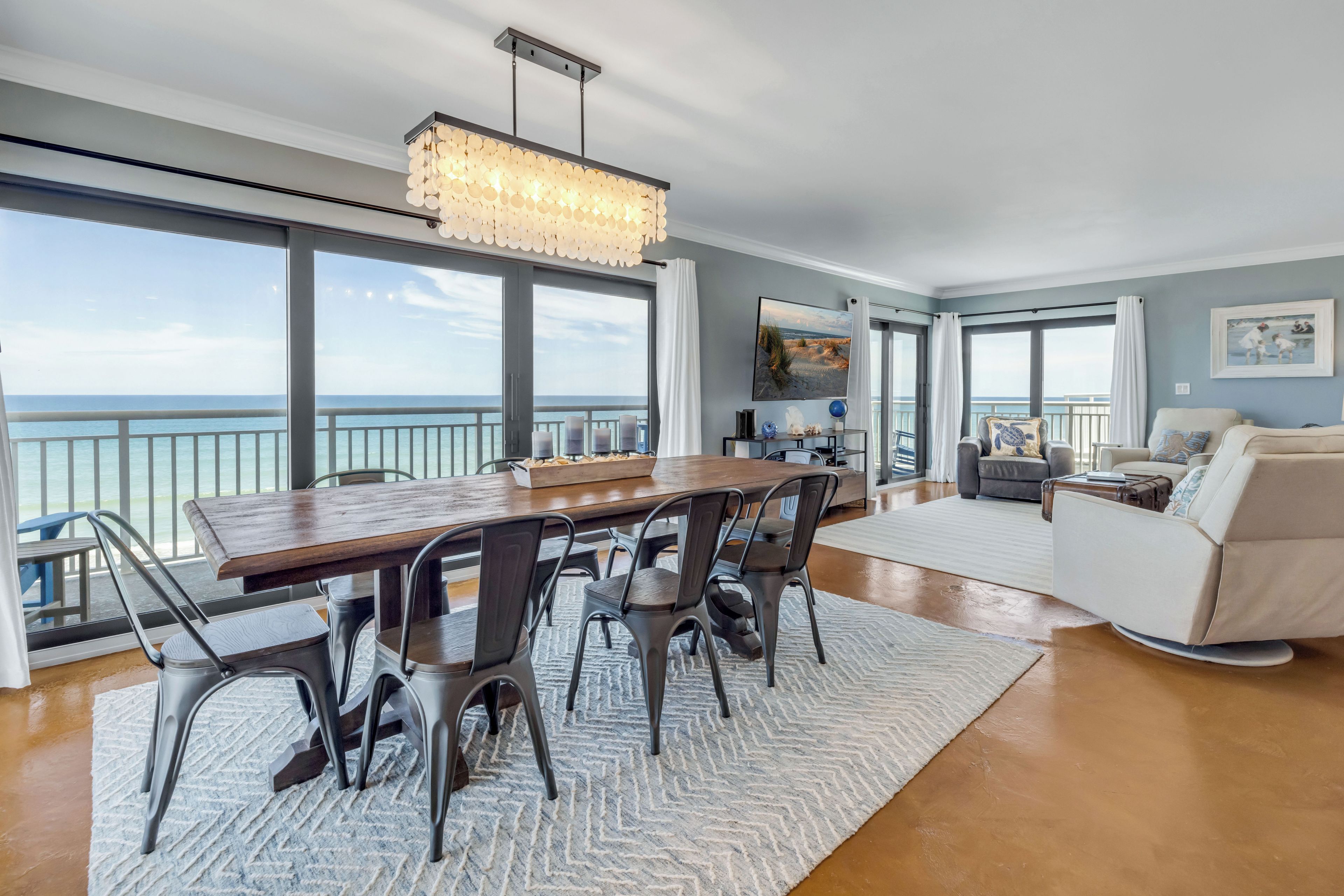 A spacious living area with a large dining table, modern chairs, a sofa, and a view of the ocean.