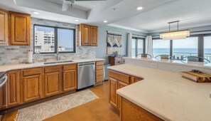 A modern kitchen with wooden cabinets, a dishwasher, and a large window overlooking the sea.