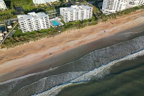 An aerial view of a beachside hotel with multiple buildings, a swimming pool, and a sandy beach.