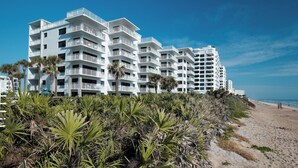 A multi-story hotel with balconies, located near a beach with palm trees. - Direct oceanfront corner penthouse with a huge wrap-around balcony and heated pool (New Smyrna Beach)
