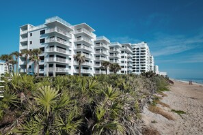 Un hotel a più piani con balconi, situato vicino a una spiaggia con palme.