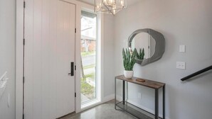 Un pasillo con una puerta blanca, una planta en maceta, un espejo redondo y una lámpara moderna.