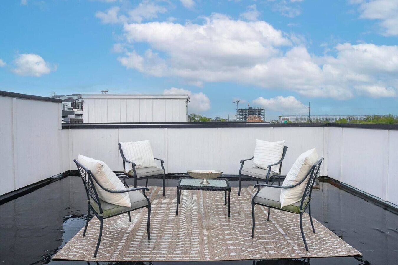 A rooftop terrace with a round table and four chairs, a patterned rug, and a view of the city skyline.