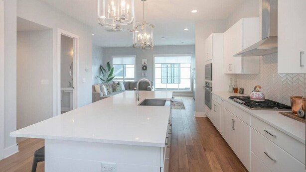 Una cocina moderna con una isla central, armarios blancos, electrodomésticos de acero inoxidable e iluminación colgante.