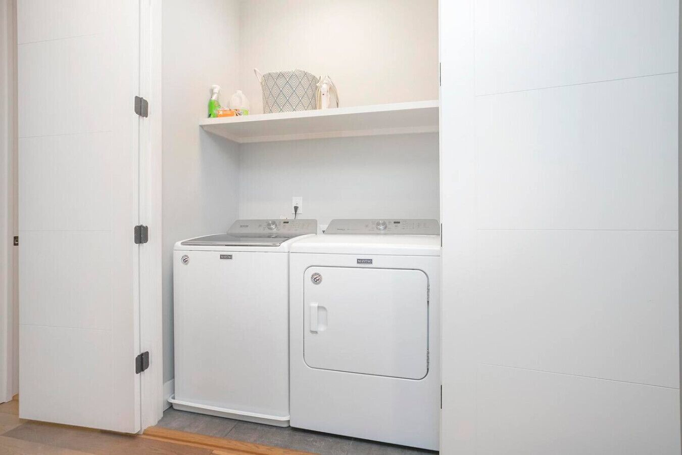 A laundry room with a washing machine and dryer, a shelf with cleaning supplies, and a door.