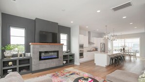 Una sala de estar moderna con chimenea, una cocina con armarios blancos y un comedor con un amplio ventanal.