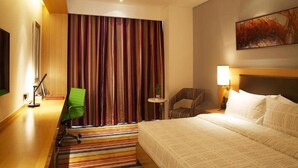 Habitación de hotel con cama, escritorio con silla, una mesita con lámpara y cortina a rayas coloridas.