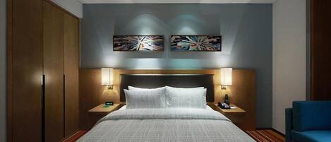 A modern hotel room with a large bed, two bedside lamps, a headboard, and two abstract paintings on the wall.