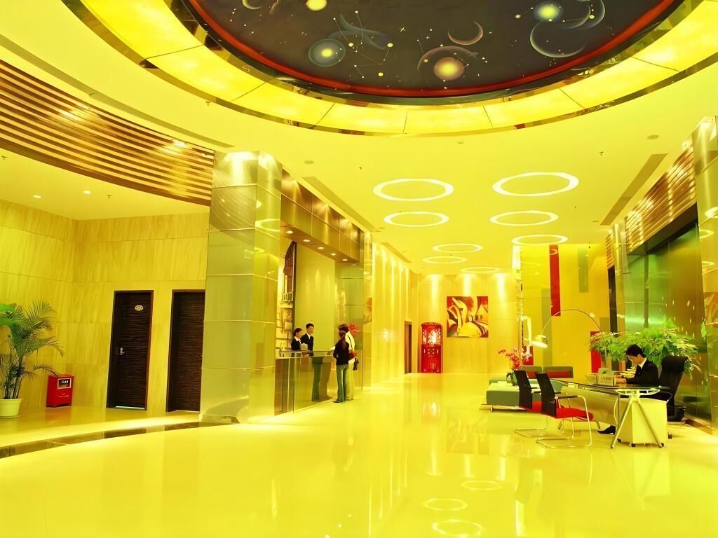 A modern hotel lobby with a reflective floor, a reception desk, and a seating area.