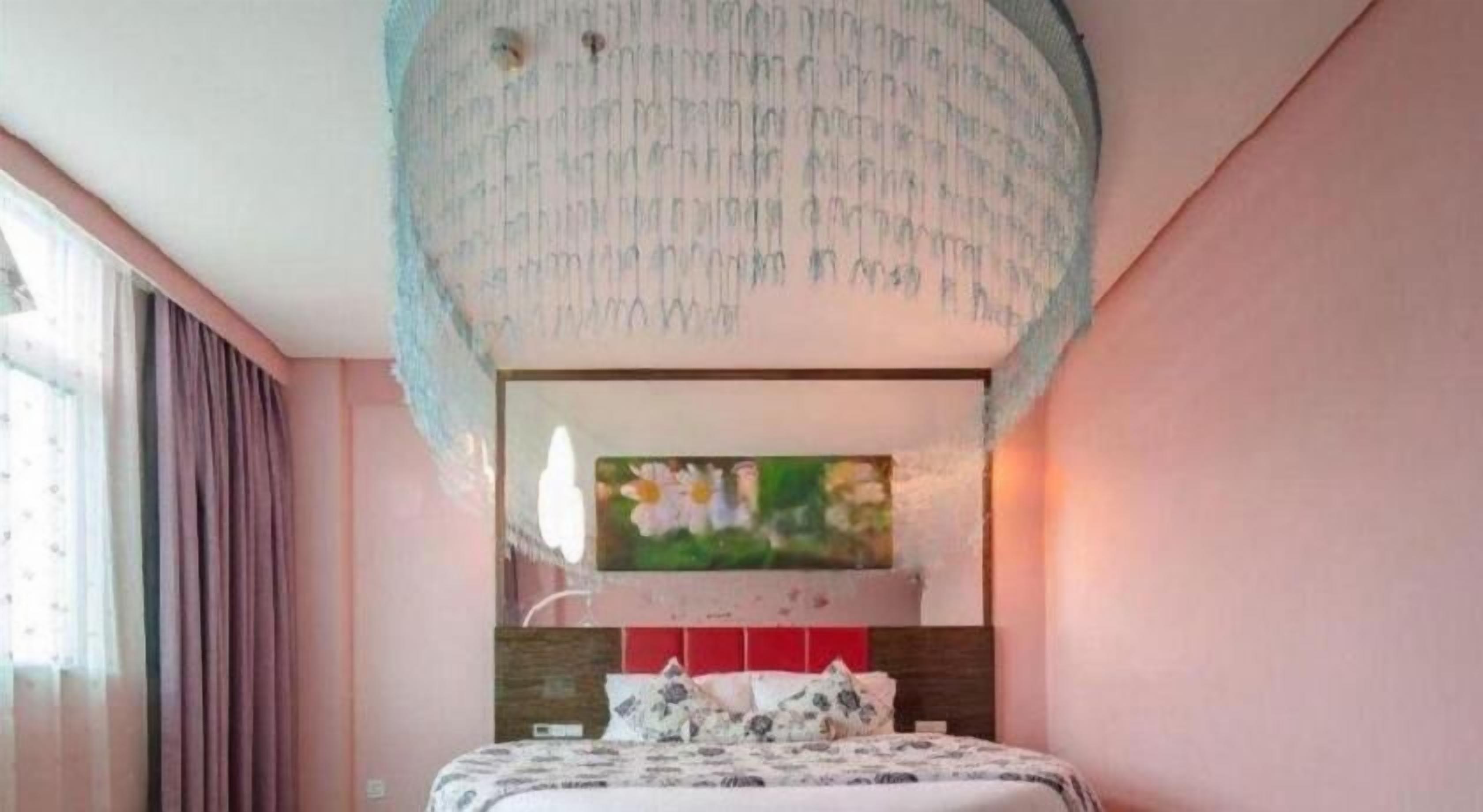 A bedroom with a bed, a painting above the bed, and a ceiling light fixture.